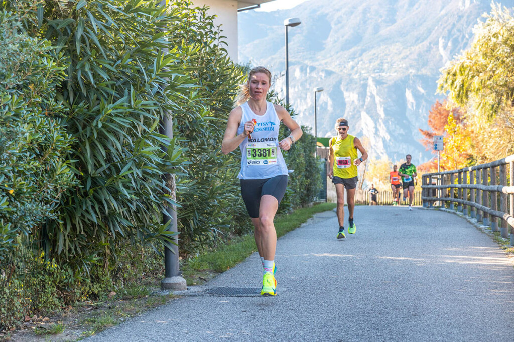 Amelie Hofbauer corre lungo il percorso della Garda Trentino Half Marathon 2024 tra Arco e Riva del Garda, con le montagne del Trentino sullo sfondo.