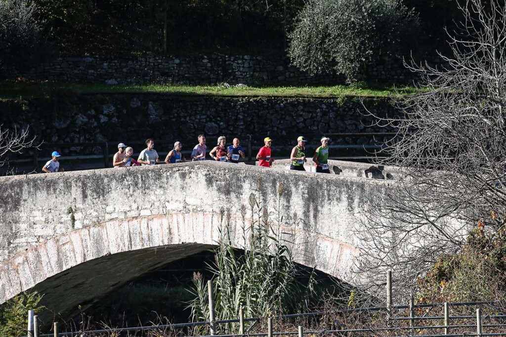 Atleti attraversano il ponte romano di Ceniga durante la Garda Trentino Half Marathon 2024, lungo il percorso che collega Arco e Riva del Garda.