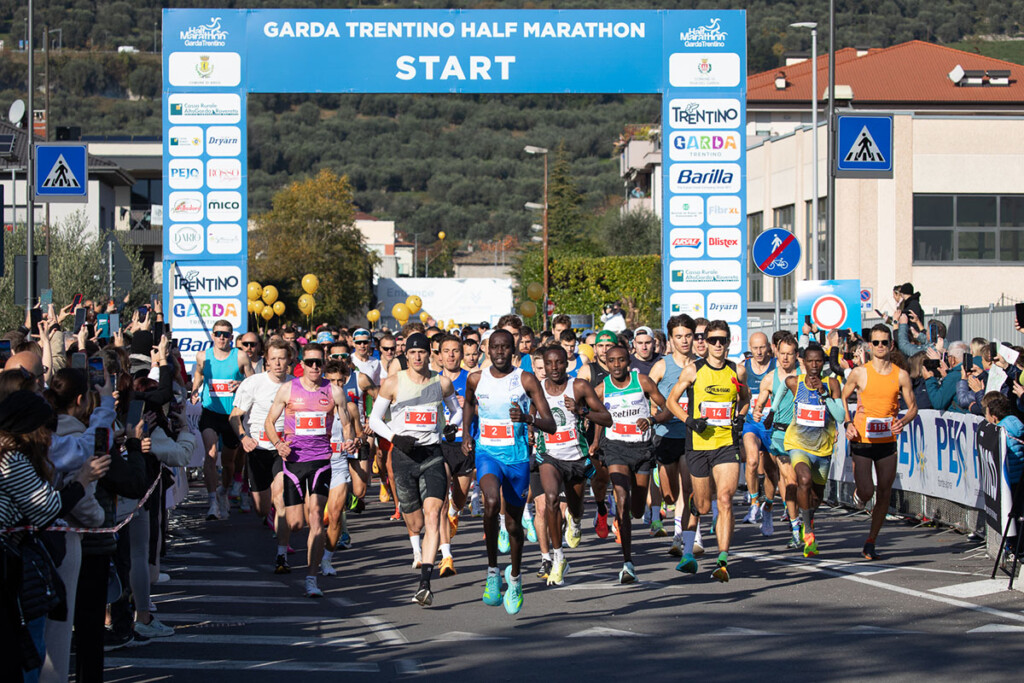 Partenza della 21 km alla Garda Trentino Half Marathon 2025 a Riva del Garda, con i top runner in prima fila sotto l’arco di start.