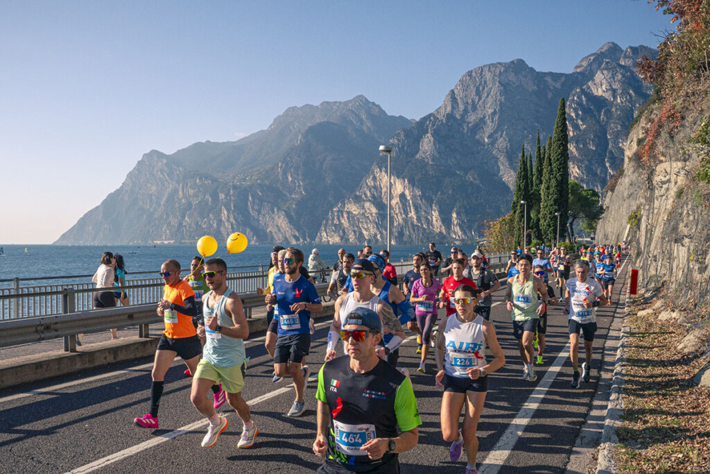 Gruppo di runner in corsa lungo il tratto panoramico di Linfano durante la Garda Trentino Half Marathon 2025, con vista sul lago e le montagne del Garda Trentino.