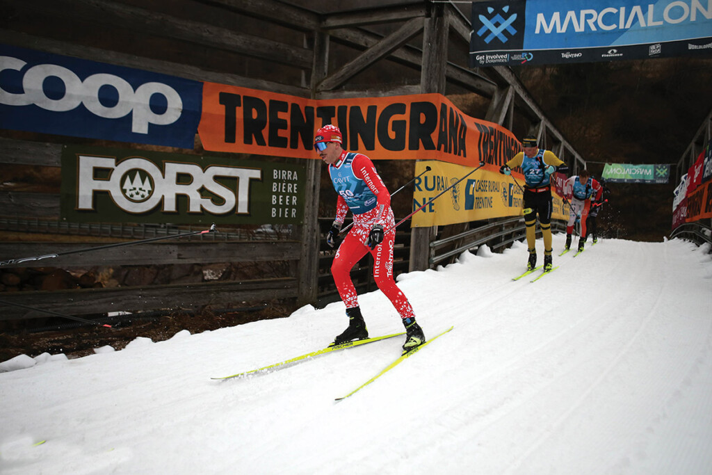 Lorenzo Busin in azione alla 52ª Marcialonga di Fiemme e Fassa durante un tratto innevato del percorso, con altri fondisti alle sue spalle e le strutture in legno del ponte gara. Photo Newspower