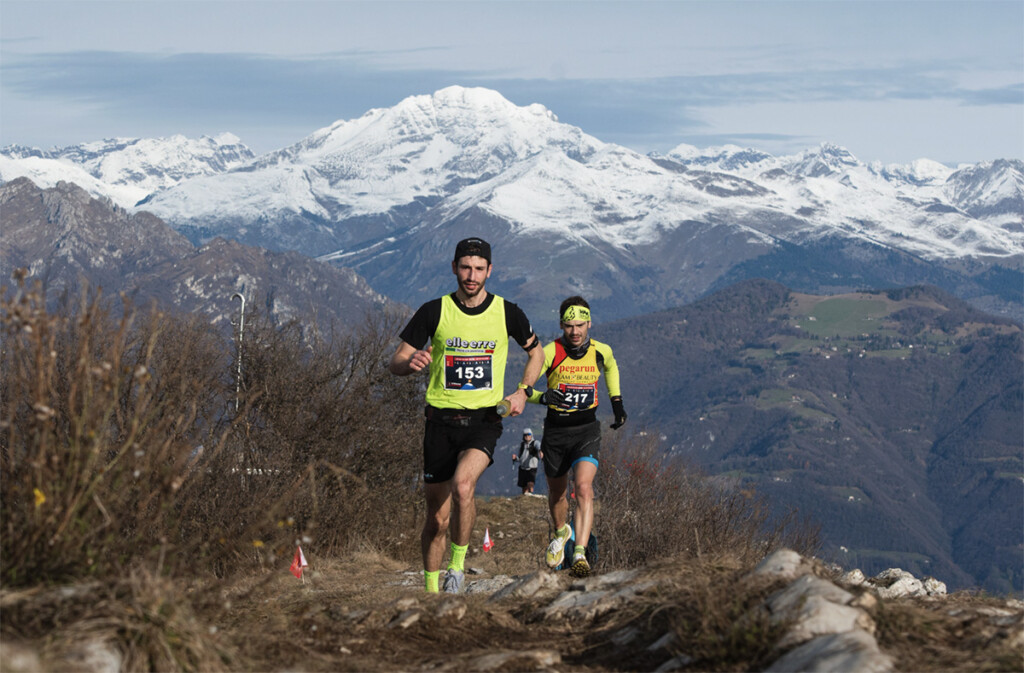 Trail runner Paolo Poli e Carlo Curnis in quota durante il Monte Misma Xmas Trail 2025 con panorama alpino innevato sullo sfondo.