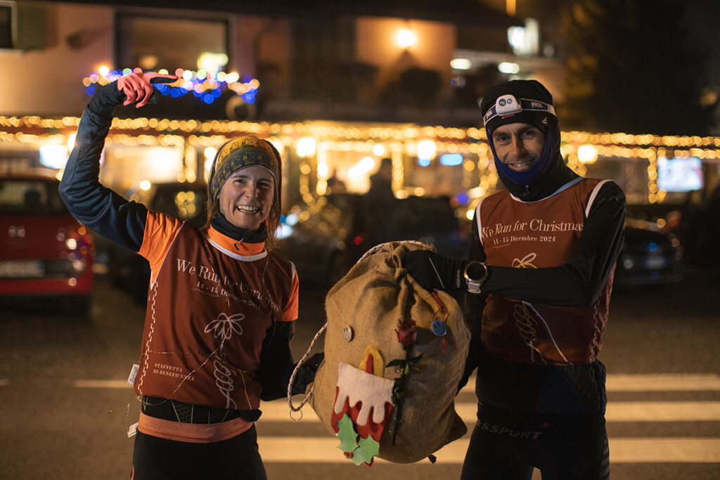 Due runner della We Run For Christmas posano con la sacca solidale durante una tappa notturna.