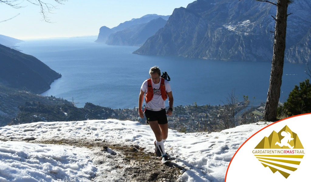 Runner sul percorso innevato del Garda Trentino Xmas Trail con vista sul Lago di Garda.