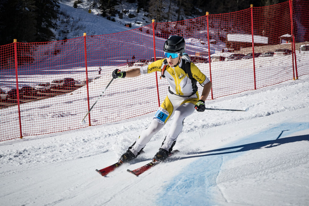 Atleta Gioele Migliorati impegnato nella fase di discesa della sprint di sci alpinismo su pista battuta, con rete di protezione sul tracciato a Madonna di Campiglio.